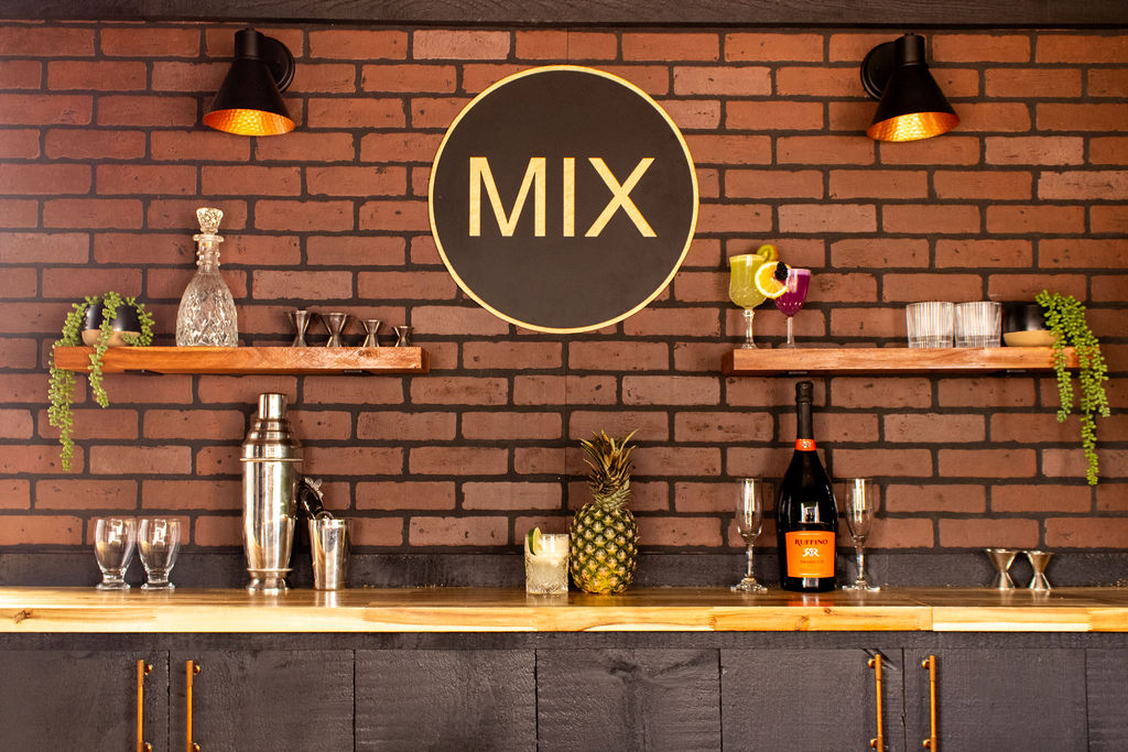A sleek black food trailer with "MIX" in large letters. Open serving window, rustic brick interior, bar counter, creating a modern and inviting vibe.
