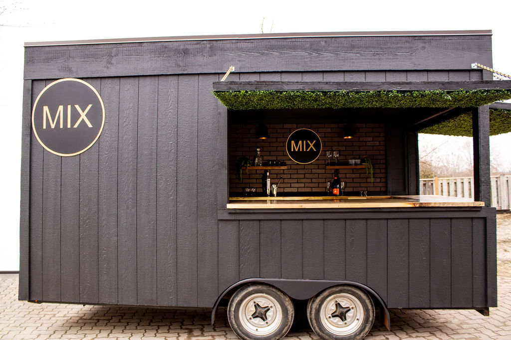 A sleek black food trailer with "MIX" in large letters. Open serving window, rustic brick interior, bar counter, creating a modern and inviting vibe.